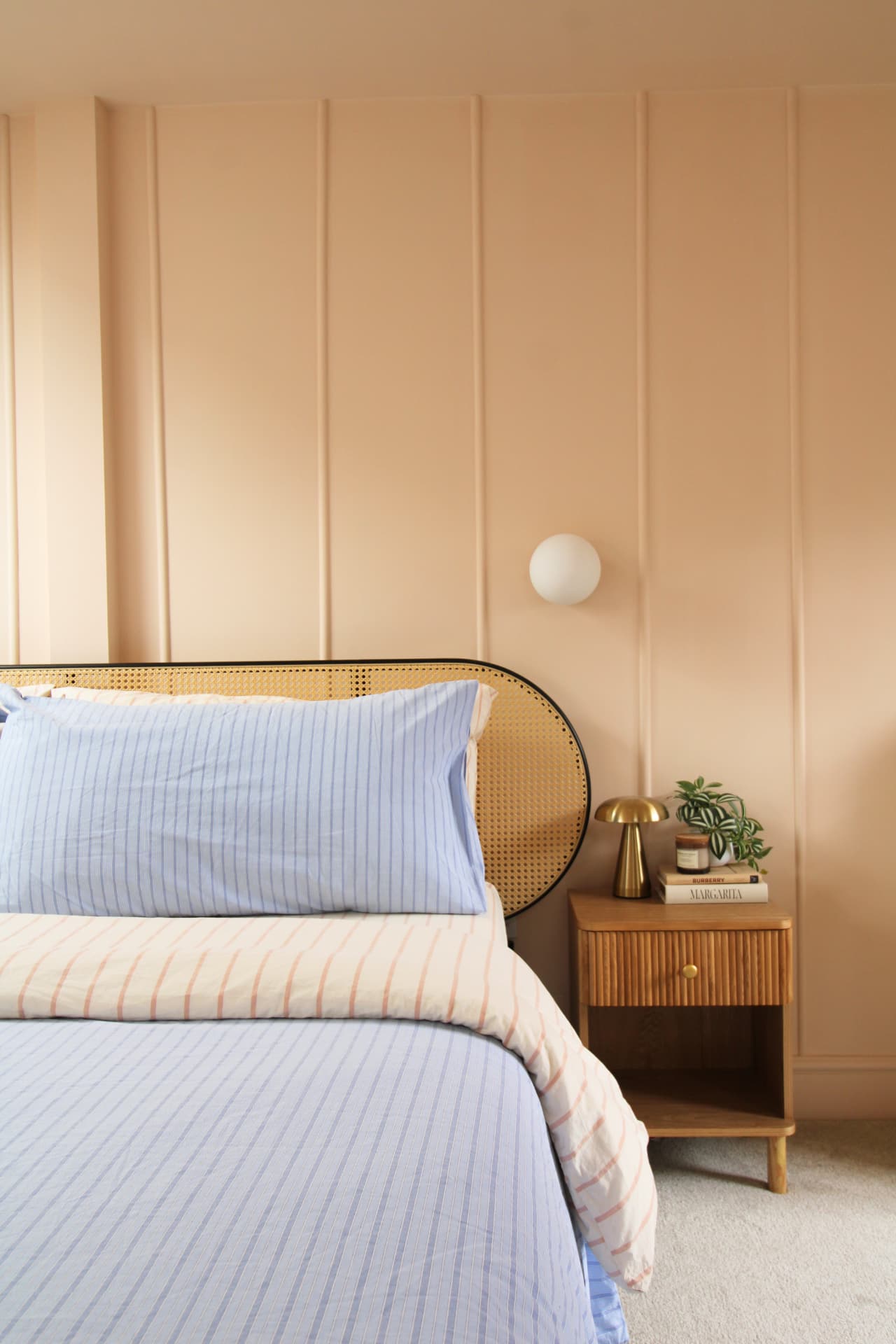 Blue striped bedding against a peach panelled wall with a rattan headboard