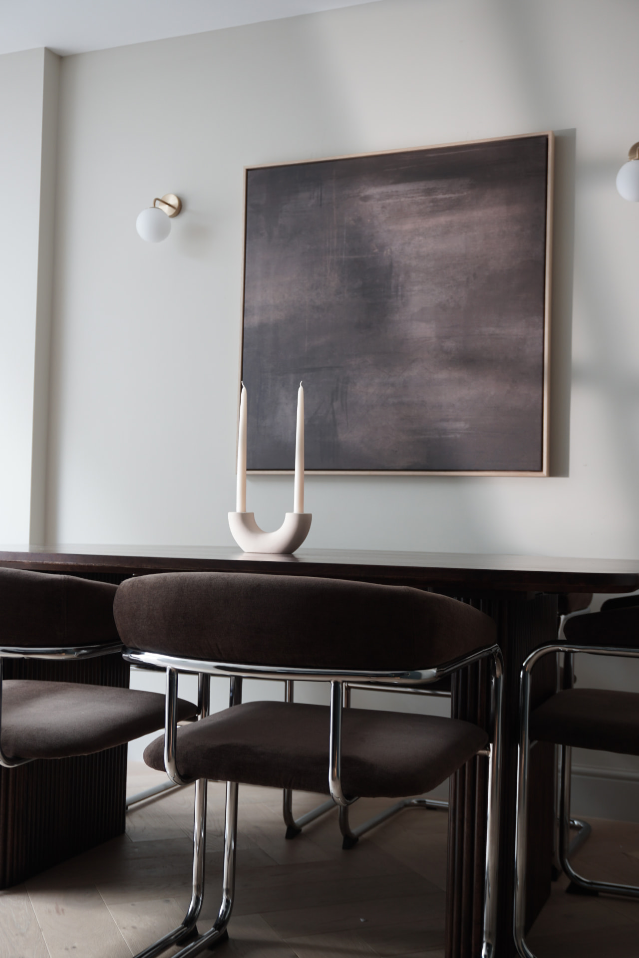 Brown velvet dining chairs under a dark abstract painting and sculptural candle holder