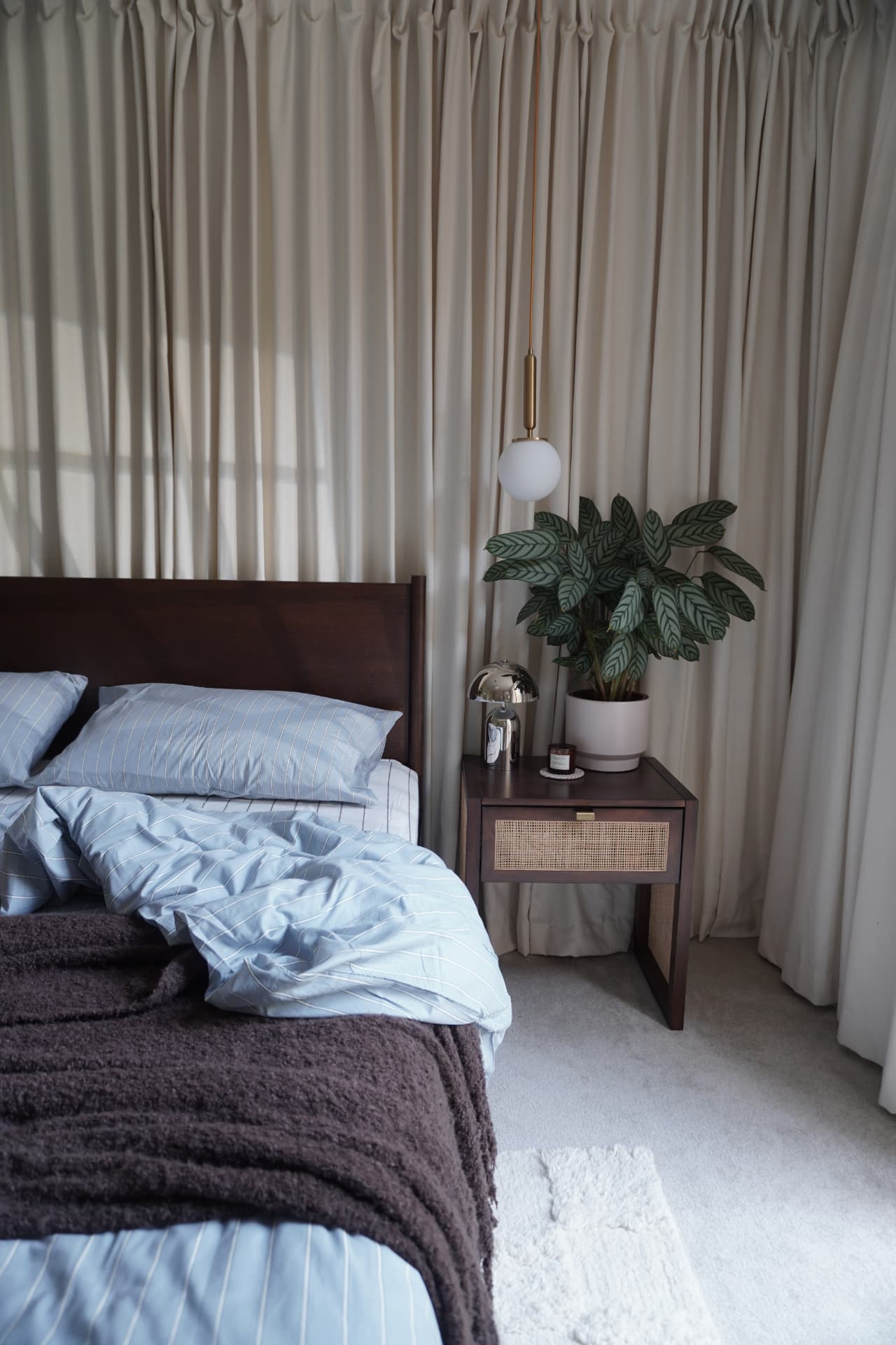 Bed with powder blue linen and a chocolate throw beside a rattan bedside table